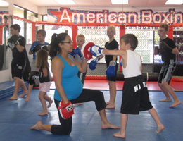 Coach Gina holds mitts for kids boxing class while pregnant.